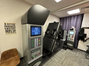 A medical treatment room with a DRX9000 spinal decompression machine, a smaller EXCITE machine, a padded treatment bed, and an inspirational sign on the wall.