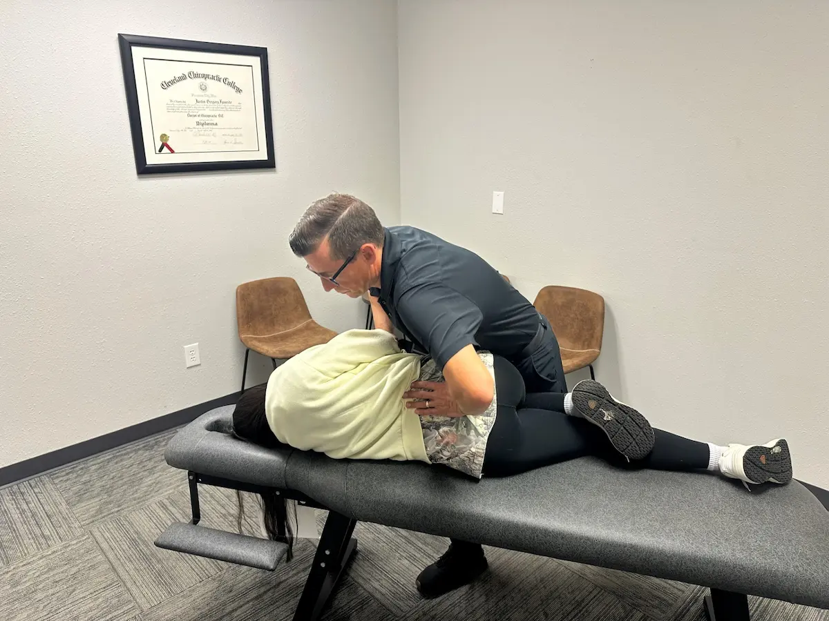 A chiropractor adjusts a patient's lower back on a chiropractic table in an office setting.