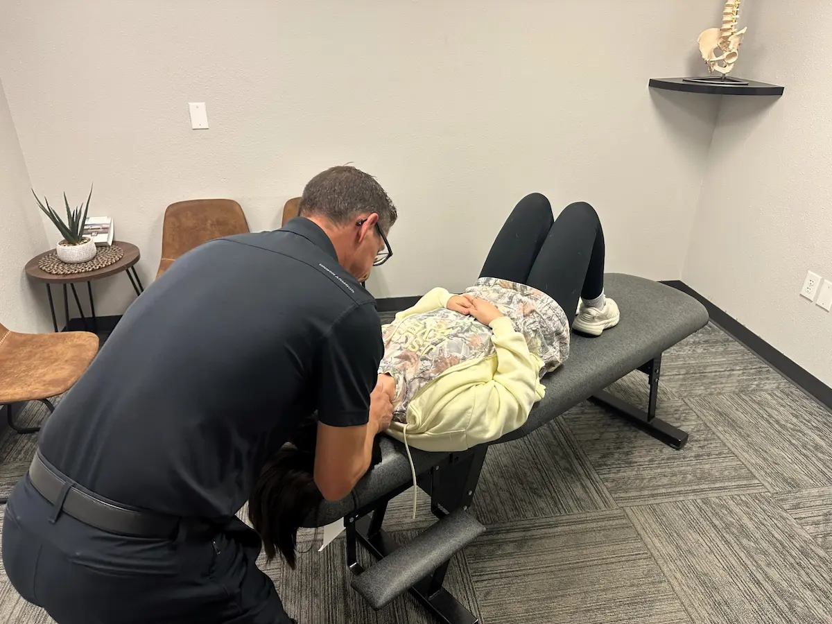 A chiropractor adjusts a patient's neck on an examination table in a clinic.