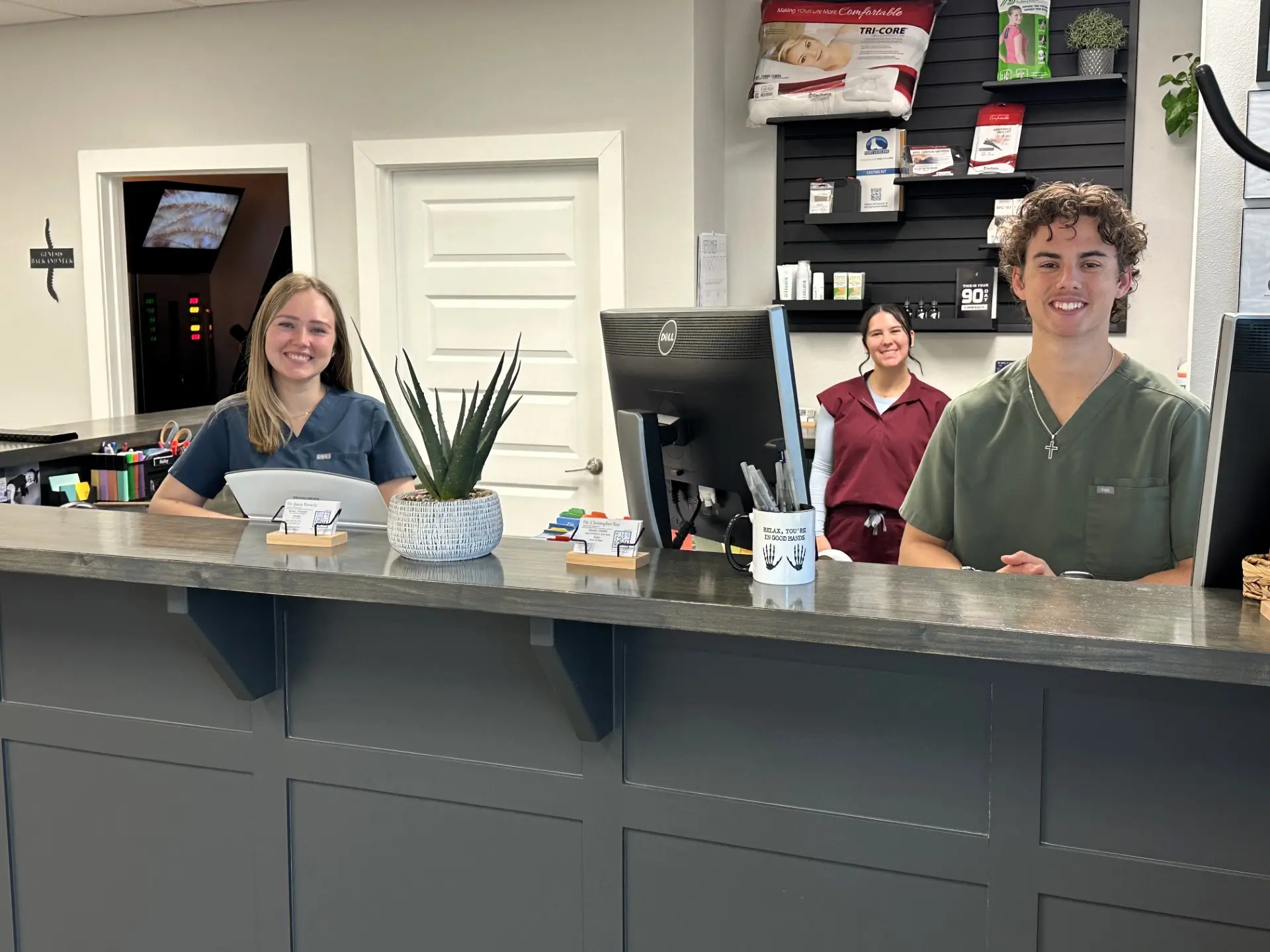 Three smiling staff members, two women and one man, stand at a modern reception desk in a clinic or office.