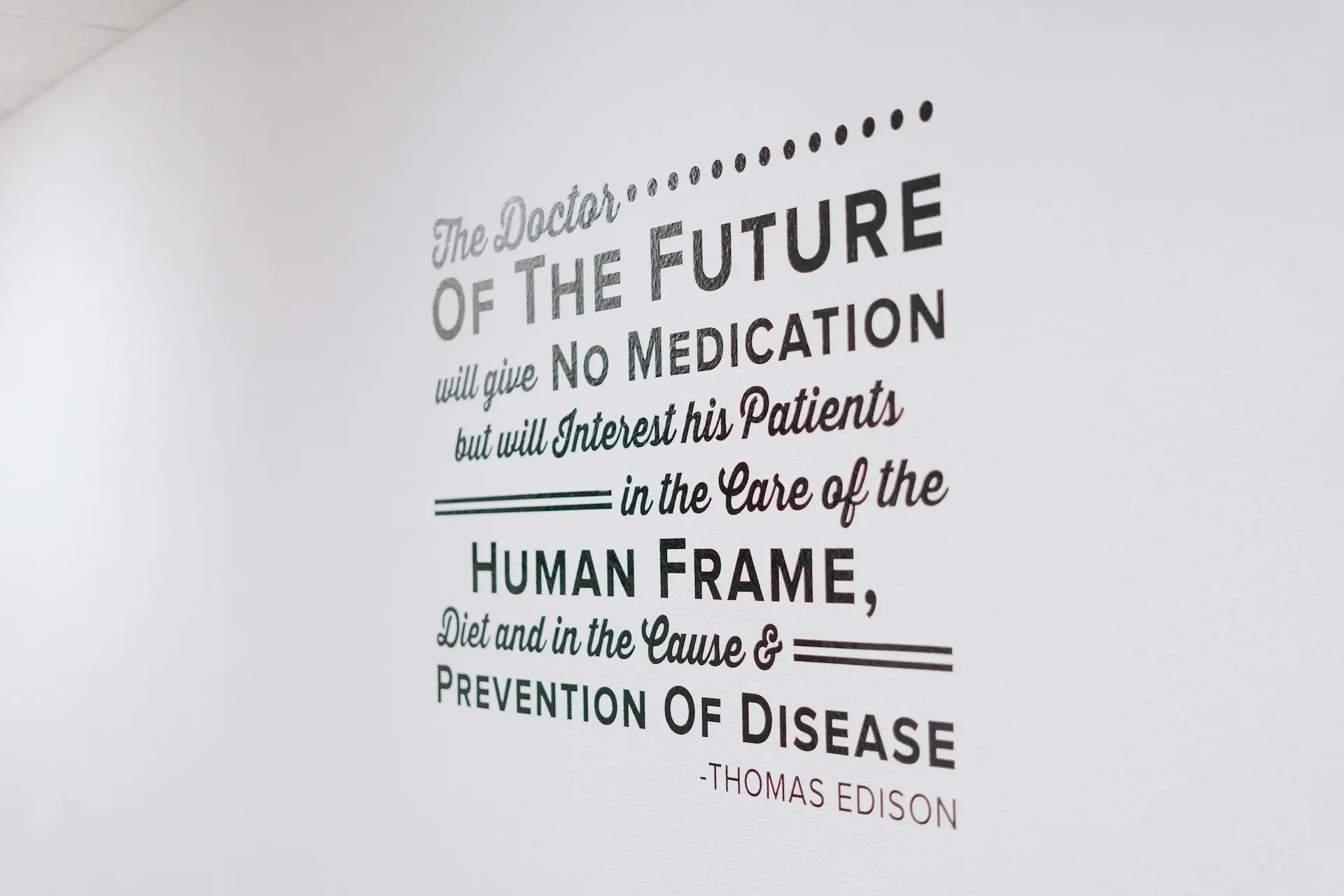 A quote by Thomas Edison on a white wall, reading: 'The Doctor... OF THE FUTURE will give NO MEDICATION but will Interest his Patients in the Care of the HUMAN FRAME, Diet and in the Cause & PREVENTION OF DISEASE'.