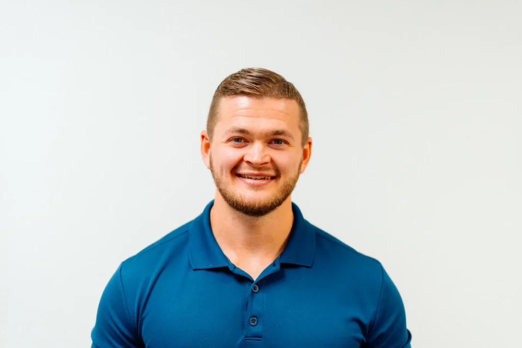 Headshot of a man smiling, wearing a blue polo shirt against a white background.
